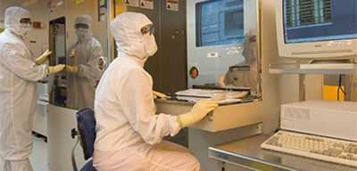 A person in a clean suit sits at a computer station while other people in clean suits work at their own lab stations. This symbolizes how Wolfspeed has many career opportunities both inside and outside of a laboratory setting.